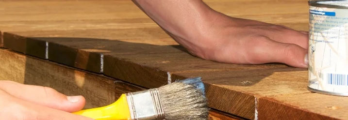 Person streicht Holzterrasse mit Pinsel